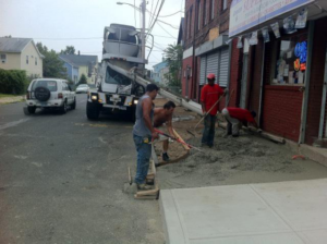 A handyman crew pouring and leveling concrete for a new sidewalk installation by Camelot Development in Bridgeport, CT.
