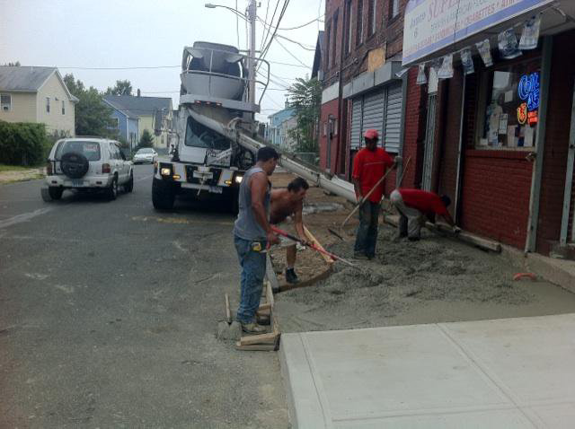 A handyman crew pouring and leveling concrete for a new sidewalk installation by Camelot Development in Bridgeport, CT.