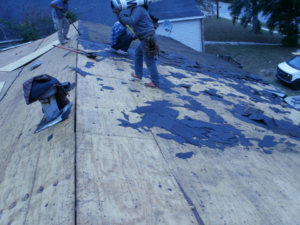 A handyman crew removing old shingles from a roof during a renovation project by John Rowland Custom Homes in Macon, GA.