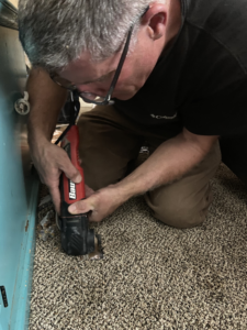 A handyman from Green River Utilities in Caldwell, ID, precisely cutting carpet with an oscillating tool.