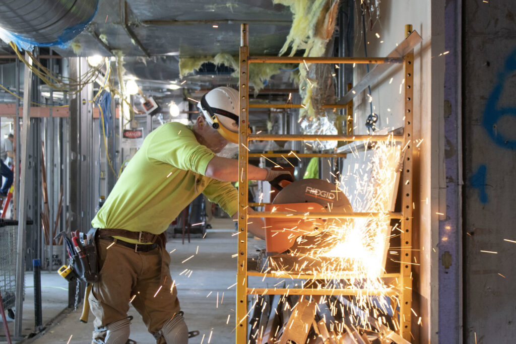 A handyman from EV Construction cutting metal with a chop saw, creating sparks, at a job site in Holland, MI.