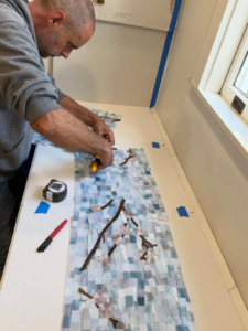 A handyman carefully cutting mosaic tiles for a kitchen backsplash project by Ayres Endeavors, LLC in New Orleans, LA.
