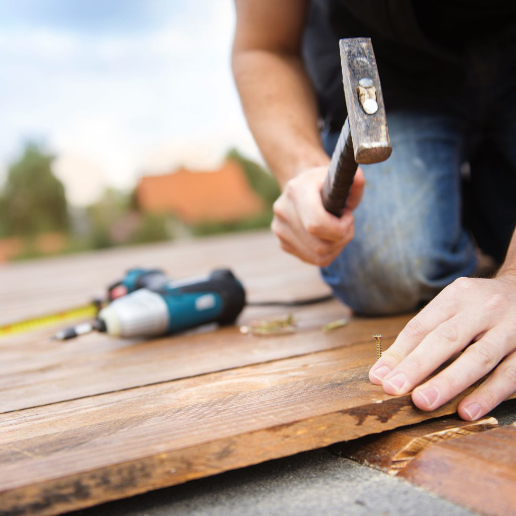 A handyman hammering a nail into a wooden board during deck repair by Louisville Handyman & Remodeling in Louisville, KY.
