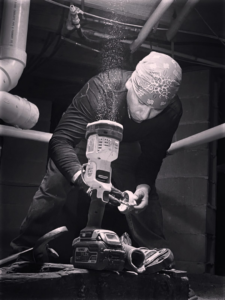 A handyman using a power drill in a dark crawlspace or basement for Sandobros Plumbing in Charleston, SC