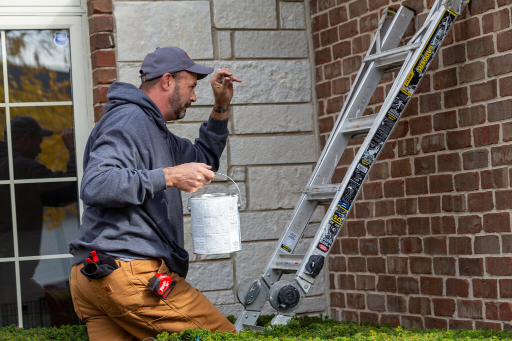 A handyman from Westlake Ace Handyman Services Kansas City Metro painting the exterior of a brick house in Lenexa, KS.