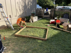 A handyman framing a wooden structure on a lawn for Anderson and Son Services in Olathe, KS