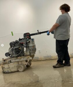 A handyman from ACT Restoration grinding a wet concrete floor as part of a restoration project in Andover, MN.