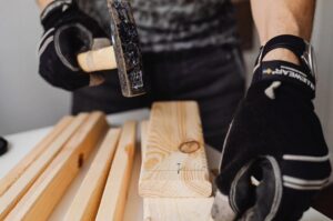 A handyman wearing work gloves, hammering a nail into a piece of wood, demonstrating services by Get It Done in Sioux Falls, SD.