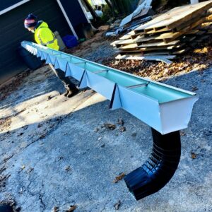 A handyman from Gutter Flow7 LLC holding a section of gutter with a downspout, ready for installation in Madison, WI.