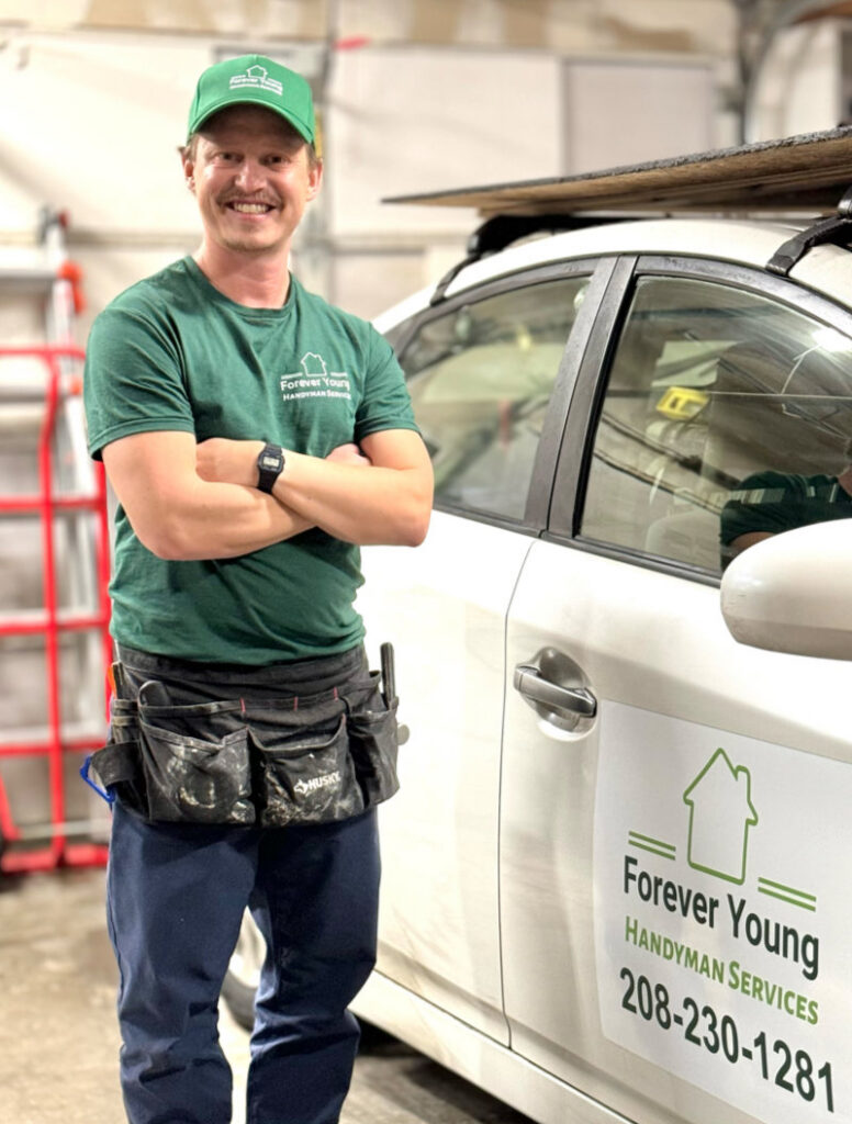 A handyman in uniform with a tool belt standing next to a branded vehicle for Forever Young Handyman Services in Boise, ID.