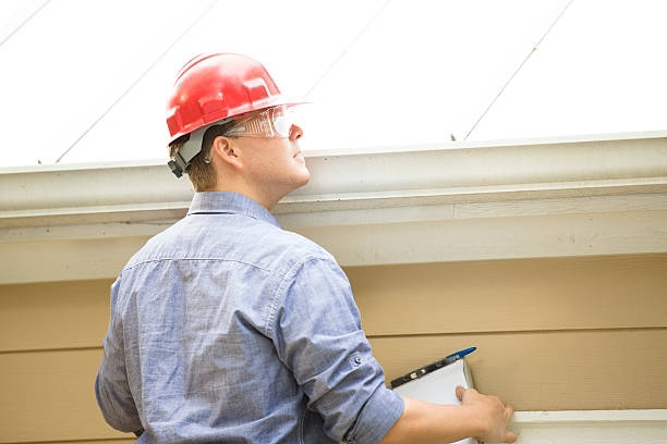 A handyman inspecting gutters and eaves with a clipboard for Chris Roofing & Remodeling Inc. in Colorado Springs, CO
