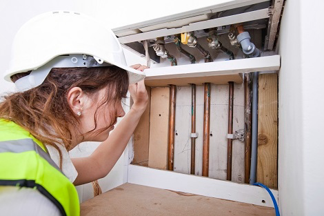 A handyman in a hard hat and safety vest inspecting exposed plumbing pipes for Advanced Mechanical Contractors, Inc. in Nashville, TN.