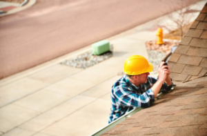 A handyman in a yellow hard hat inspecting a shingle roof for Chris Roofing & Remodeling Inc. in Colorado Springs, CO