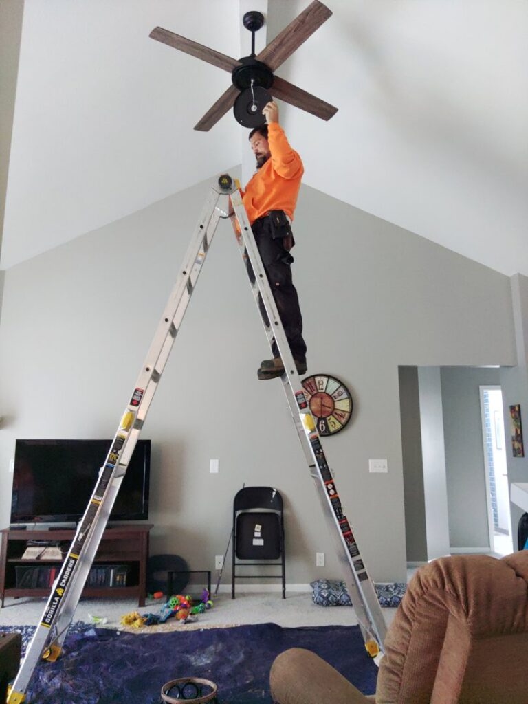 A handyman from IFixdIt Handyman Services in Omaha, NE, on a ladder installing a new ceiling fan.