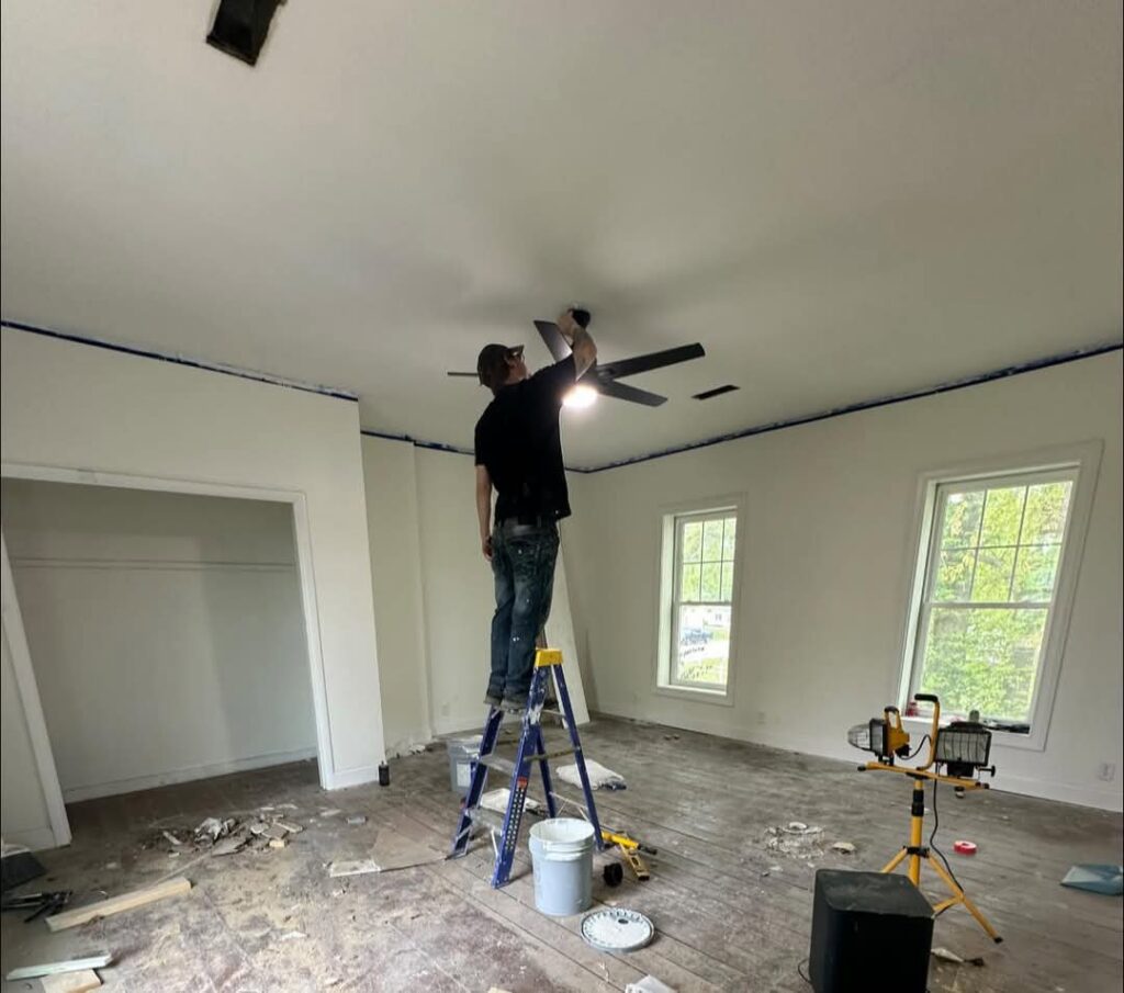 A handyman from Imperial Access Contracting installing a new ceiling fan in a room under renovation in Evansville, IN.