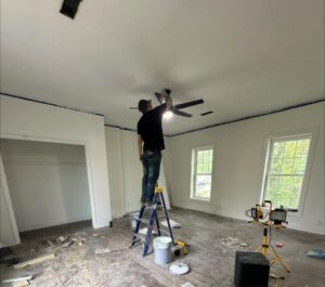 A handyman from Imperial Access Contracting installing a new ceiling fan in a room under renovation in Evansville, IN.