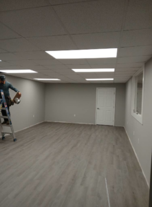 A handyman on a ladder installing ceiling tiles or lighting in a newly remodeled room by Quiros Remodeling in Greenville, SC.