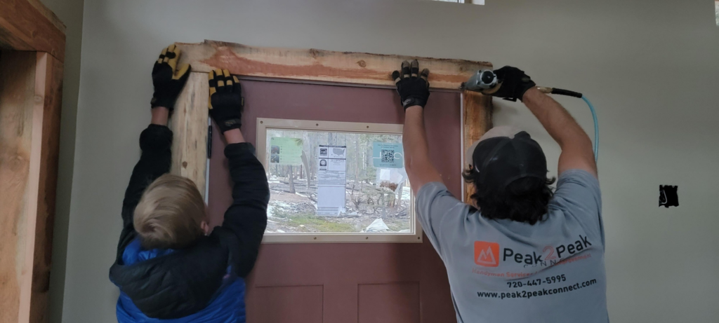 Handyman using a nail gun to install door trim, showcasing services by Peak2Peak Connect Handyman Services LLC in Arvada, CO.