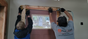 Handyman using a nail gun to install door trim, showcasing services by Peak2Peak Connect Handyman Services LLC in Arvada, CO.