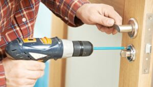 A handyman installing a new doorknob with a power drill for Honey Bee's Handyman Services in Hastings, NE.