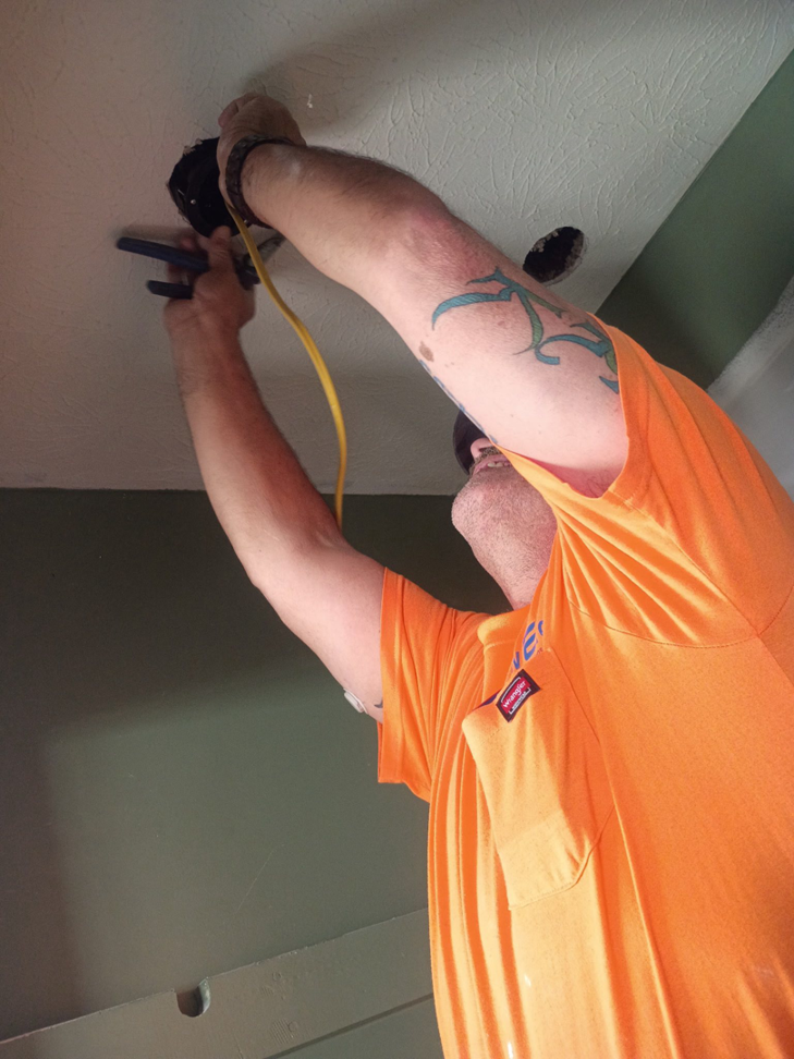 A handyman installing electrical wiring in a ceiling, performing electrical services for NewEra Construction & Solutions in Lexington, KY
