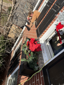 A handyman installing exterior holiday decorations on a house window box for Kaufman Construction in West Des Moines, IA.