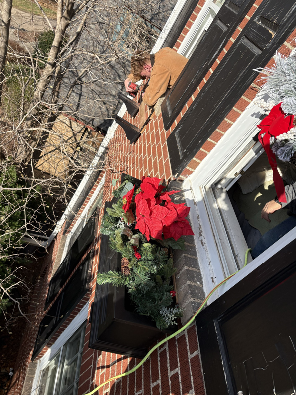 A handyman installing exterior holiday decorations on a house window box for Kaufman Construction in West Des Moines, IA.