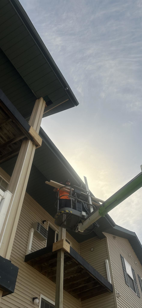 A handyman installing exterior siding from a lift on a building project by New Life Custom Carpentry in Livonia, MI.