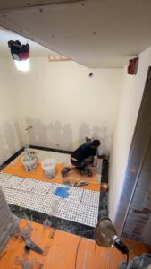A handyman installing floor tiles in a room, showcasing work by Infinite Creations Construction, LLC in Denver, CO