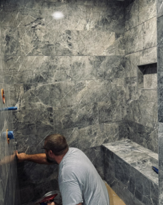 A handyman from Kizer Construction installing dark grey marble-look tiles in a shower in Owensboro, KY.