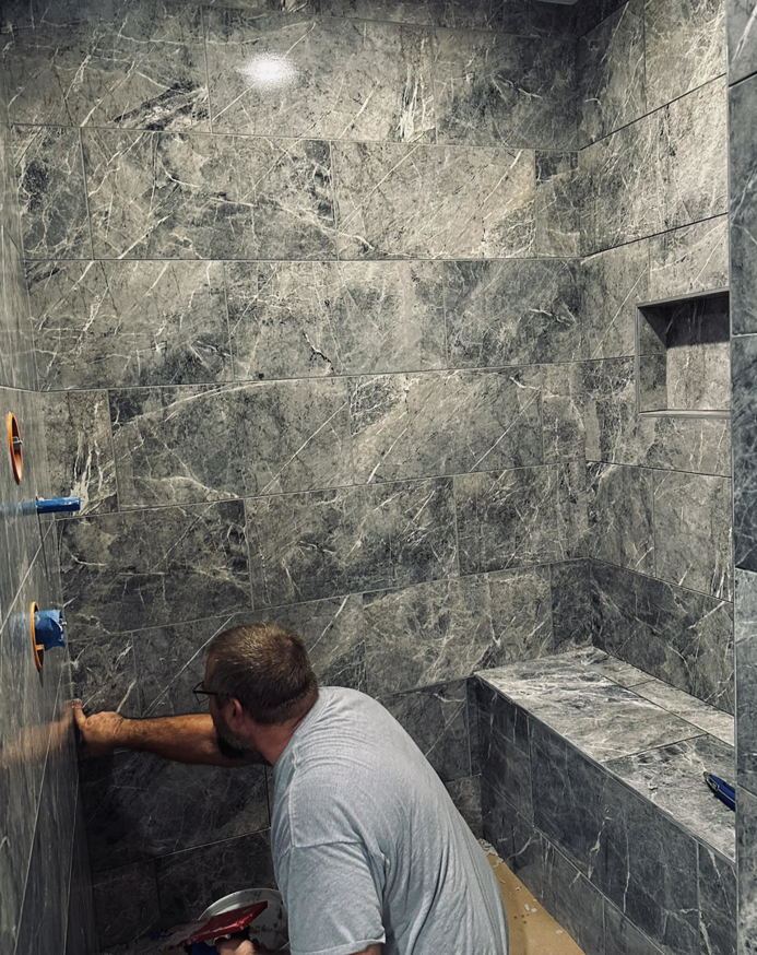 A handyman from Kizer Construction installing dark grey marble-look tiles in a shower in Owensboro, KY.