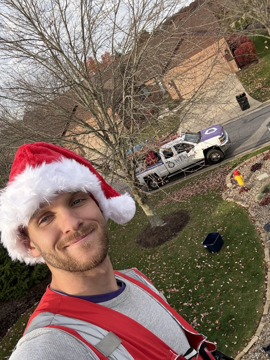 A handyman in a Santa hat and safety harness installing holiday lights on a roof for Ohio Holiday Lighting in Akron, OH.