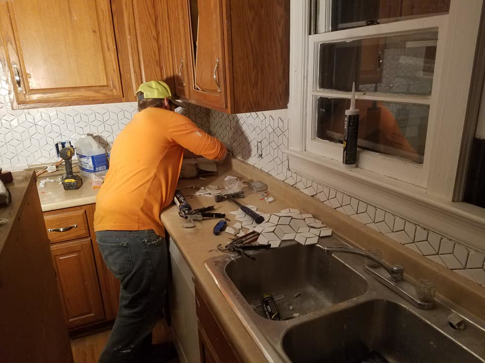 A handyman installing geometric backsplash tiles in a kitchen, a service provided by Clayton's Remodeling And Home Services in Vero Beach, FL.