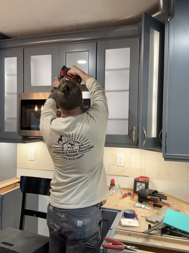 A handyman from Affordable Home Solutions installing kitchen cabinets and appliances in Springfield, PA.