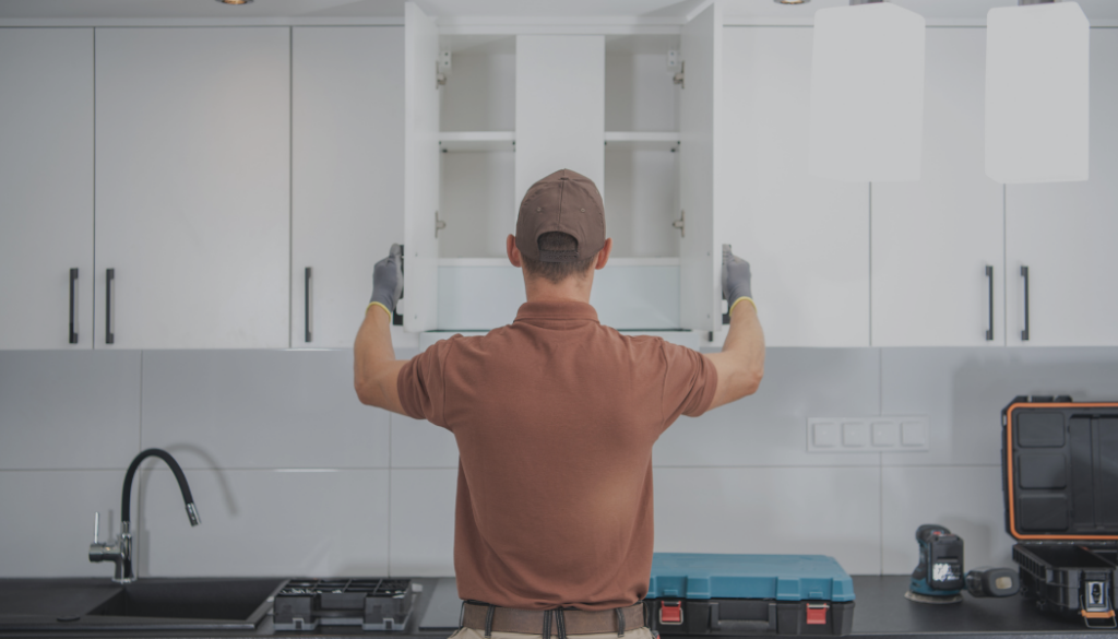 A handyman installing or adjusting white kitchen cabinets, showcasing property solutions by Kirkland Residential & Property Solutions in Clarksville, TN