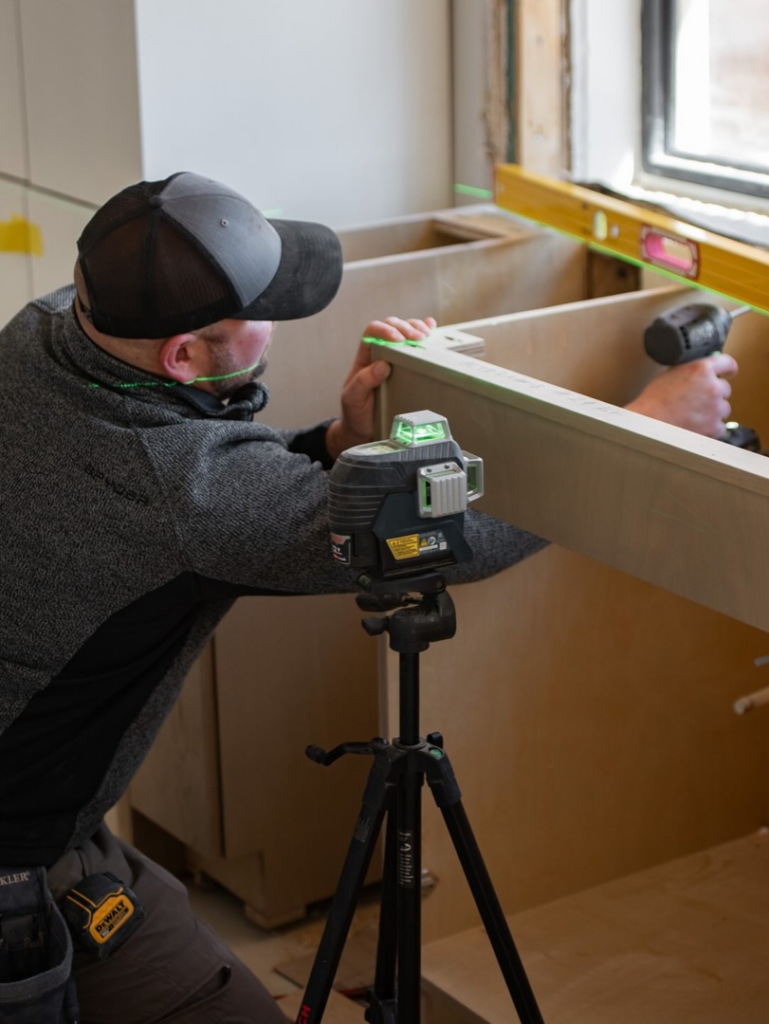 A handyman installing kitchen cabinets with a laser level for South Haven Builders in Athens, GA
