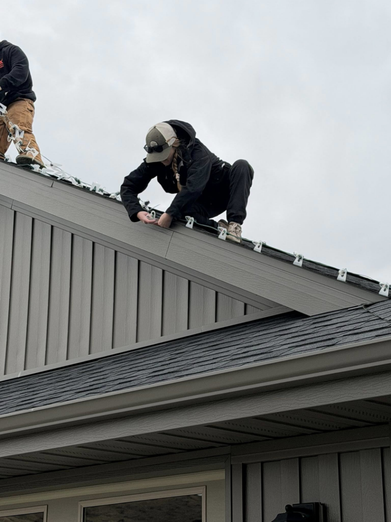 A handyman carefully installing outdoor lights on the roof of a house, a service offered by JP Handyman Wyo in Sheridan, WY
