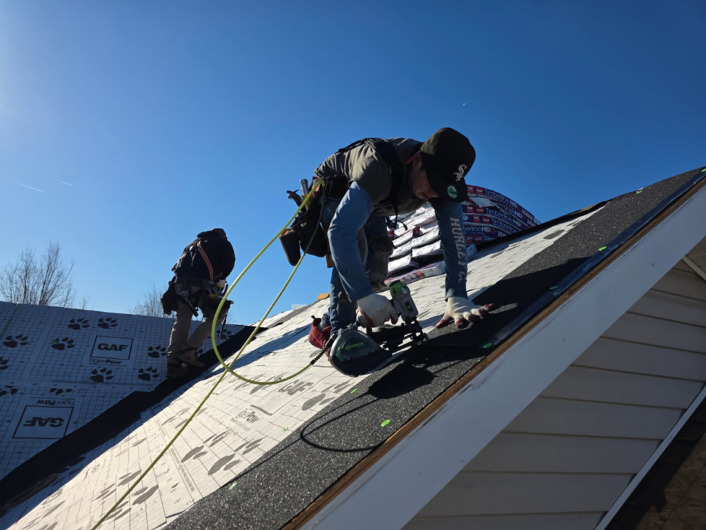 A handyman installing roof shingles with a nail gun on a residential property for Bayside Exteriors in Lewes, DE.
