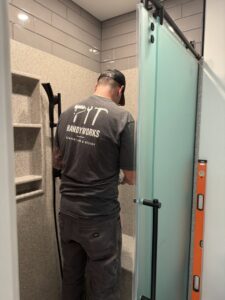 A handyman from Handyworks by Cody English installing a shower door and fixture in a modern bathroom in Cedar Rapids, IA