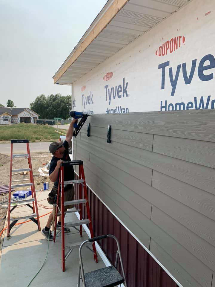 A handyman installing new siding on a house with a nail gun for Simmons Handyman Services & Contracting LLC in Billings, MT
