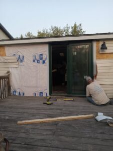 A handyman installing siding next to a sliding glass door on a deck, a project by The Creative Carpenter in Minot, ND.