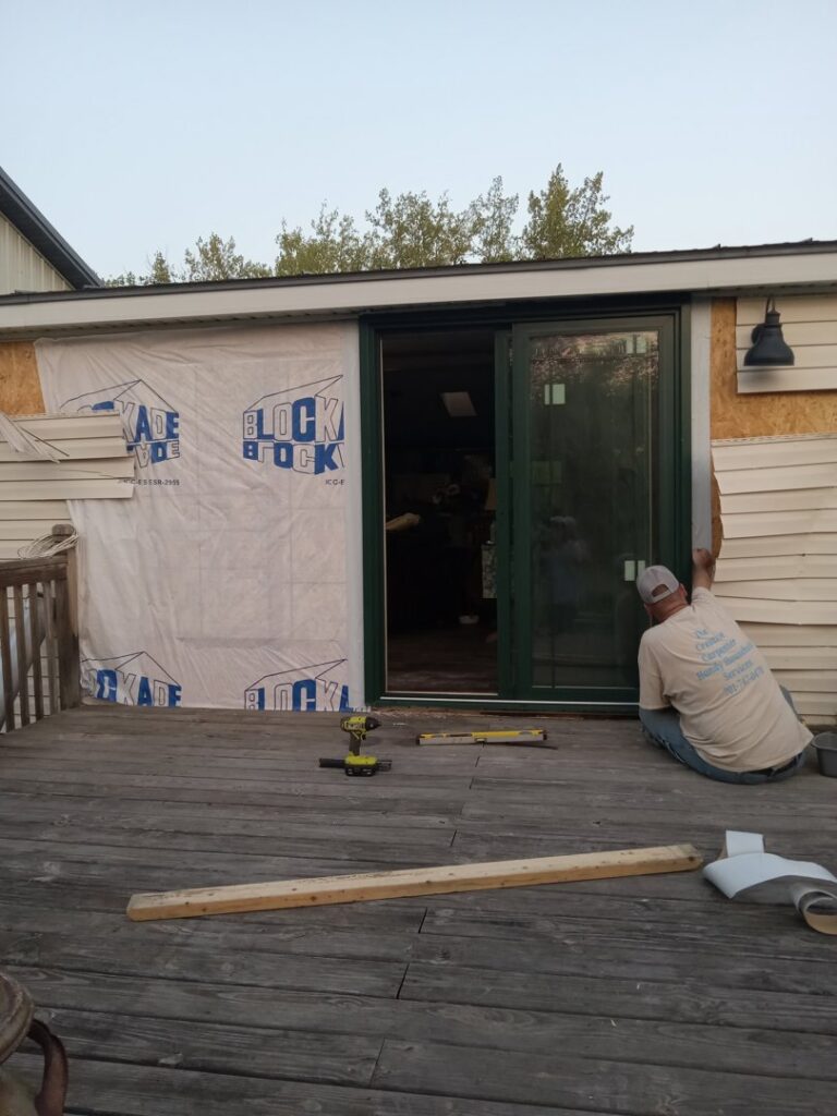 A handyman installing siding next to a sliding glass door on a deck, a project by The Creative Carpenter in Minot, ND.