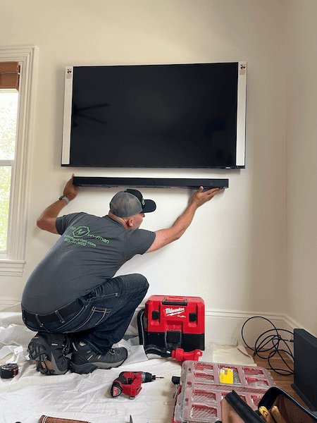 A handyman from Triple M Handyman installing a soundbar below a wall-mounted TV in Portsmouth, NH.