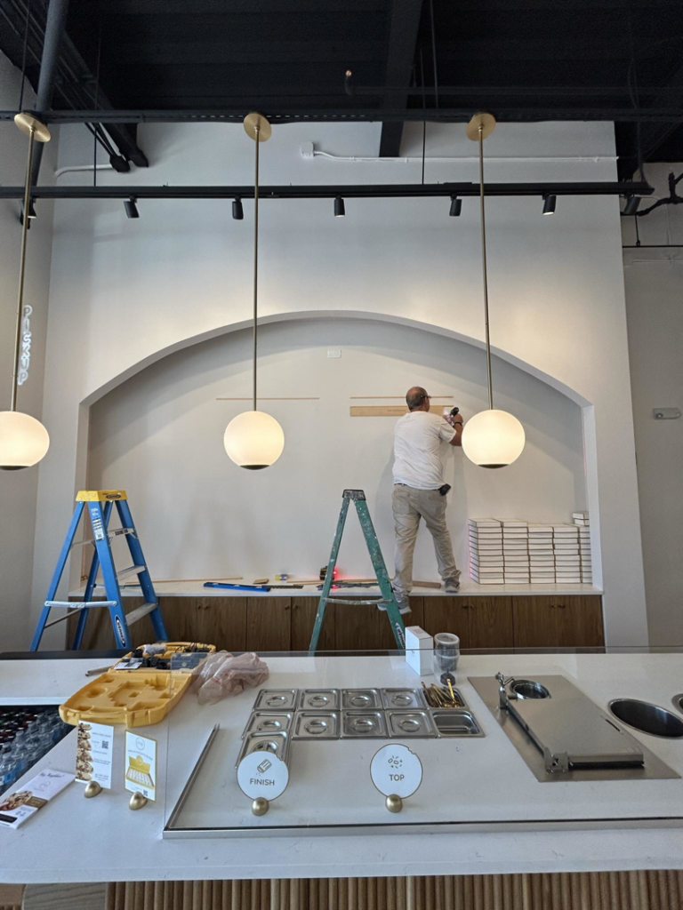 A handyman from Beck & Company Construction installing trim or shelving on a wall in a commercial space in Northport, AL.