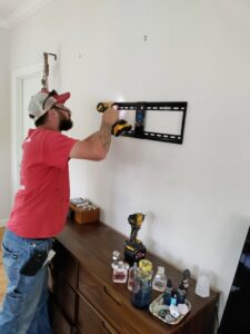A handyman installing a TV wall mount on a white wall using a drill, a common service by Homefix Lawrence in Lawrence, KS.