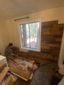 A handyman from The Handy Nevadan LLC installing decorative wooden wall paneling next to a window in Reno, NV.