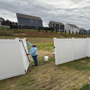 A handyman installing a white vinyl fence gate for a client of Tim's Fencing in Knoxville, TN.
