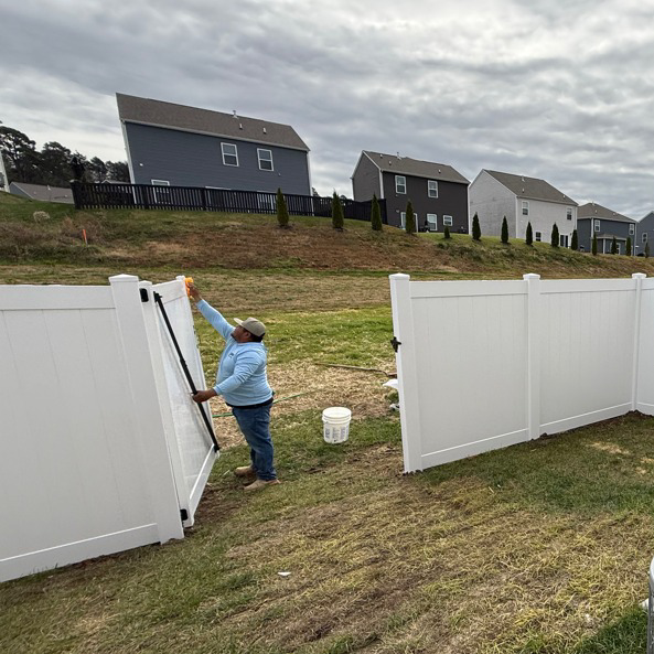 A handyman installing a white vinyl fence gate for a client of Tim's Fencing in Knoxville, TN.