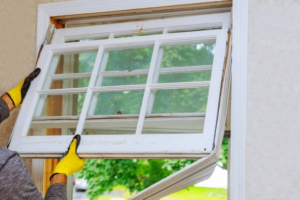A handyman in yellow gloves installing a window sash, a service offered by B&S Home Improvement in Evansville, IN.