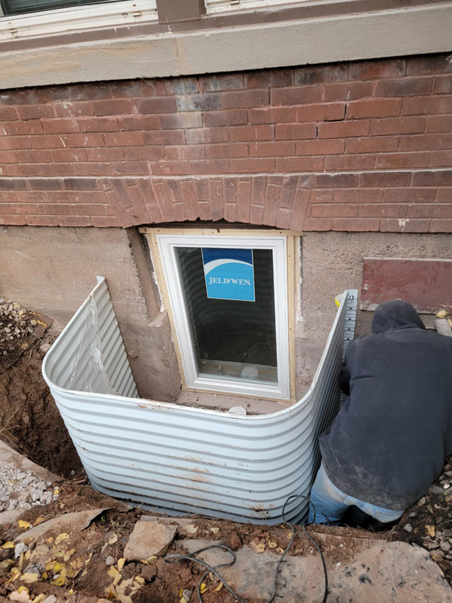 A handyman installing a new window well and basement window for a home, by Zambrano Concrete in Duluth, MN.